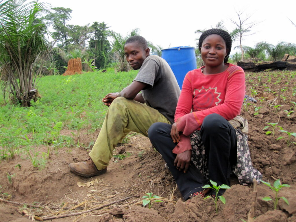 Two people sit by a carrot field in Ghana