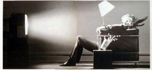 A person reclines in a chair, bathed in the glow of a television set, with a lit lamp behind them — captured in black and white in an old Maxell advert. The scene suggests they're being pushed back in their chair by the sound.